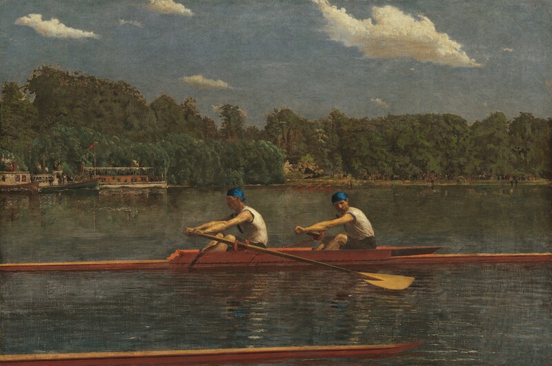 Two men with pale skin, wearing white sleeveless shirts and royal-blue caps, row in unison in a long, narrow boat on a placid blue river in this horizontal landscape painting. The low, honey-colored wooden boat extends off both sides of the canvas. Both men face our left as they row to our right. The man in front looks ahead of him, beyond the stern of the boat, and the man to our right, closer to the bow, tucks his chin down to look past his shoulder. Their bare, muscled arms are extended straight as the two oars sweep back. The tip of another boat runs close and parallel to the bottom edge of the composition, spanning the left three-quarters of the painting. The opposite riverbank is lined with a dense forest of pine-green trees. People crowd along the decks of a steamboat and a paddleboat near the riverbank to our left. Another narrow skuller, rowed by four people wearing ruby-red shirts, cuts through the water at the back center of the river. The riverbank beyond is lined with people, painted with strokes of black and white, and minuscule touches of red. The horizon comes halfway up the composition. Cream-white clouds float across a muted, topaz-blue sky above the trees.