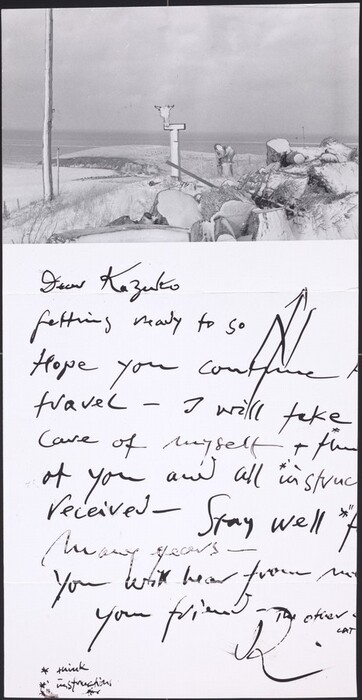 This is a photograph showing a snowy landscape with a handwritten letter overlaid. The image features a desolate, snow-covered scene with various piles of rocks and wood covered in snow in the foreground. A single pole with an animal skull mounted on it is also visible. A snow-covered hill stretches towards the horizon where an ocean meets the sky. The lower half of the image contains the handwritten letter, beginning with "Dear Kazuko," and expressing sentiments on travel and well-being before ending with a signature. The handwriting is distinctive and cursive, with annotations and asterisks for clarification.