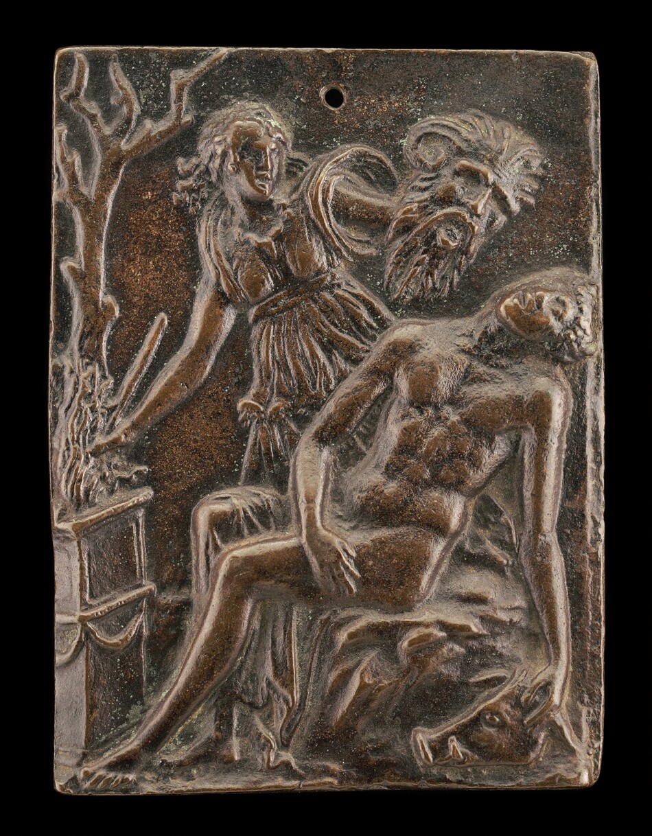 The sculpture depicts three figures in a relief format on a rectangular plaque. The central figure appears to be a person in a reclined position, supported by another figure who is standing. The standing figure is dressed in draped clothing and extends an arm towards a tree on the left side of the composition. To the right of this standing figure, there is a bearded face emerging from the background, observing the scene. The sculpture is crafted from a material that resembles bronze or a brownish metal. The plaque has a small hole near the top center. The figures are portrayed with a high level of detail, allowing viewers to discern facial expressions and clothing textures despite the compressed space of the relief.