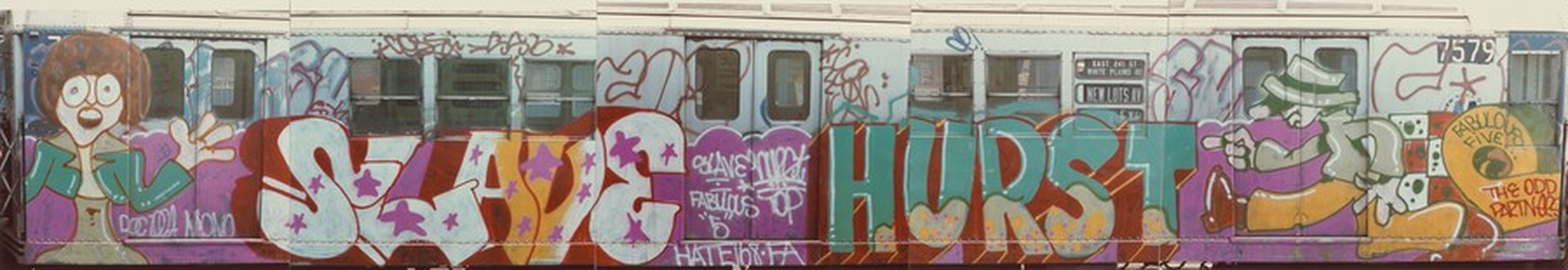 This is a photograph of a subway train covered in graffiti art. The train's exterior is adorned with vibrant and colorful graffiti, which includes cartoon-like characters, bold text, and abstract shapes. The left side shows an illustration of a person with large eyes and a surprised or excited expression, wearing a green jacket and standing in front of a purple background. Beside this character is the word "LOVE" in large bubble letters filled with purple stars set against a red and orange background. To the right is the text "HURST" in colorful letters that are blue with yellow accents. The right side of the train features another cartoon character, this time holding a paint roller or a large brush, dressed in a green and white outfit and wearing a green hat. Smaller tags and phrases like "Fabulous Five" and "The Odd Partners" are scattered across the scene.