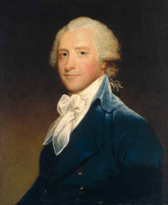 Shown from the chest up, a pale-skinned, clean-shaven man wearing a sapphire-blue coat over a white cravat looks out from this vertical portrait painting. The man’s body is angled to our left, but he turns his face to look at us from the corners of his gray eyes. His smooth cheeks are flushed, and he smiles slightly. His white hair, probably a wig, sweeps back from his forehead and curls over his ears. His snow-white cravat is tied in a bow, and the pointed ends of the fabric fall over the wide lapels of his coat. The man is lit from our right, and a sheen on the high collar suggests velvet. Brass buttons gleam on the front of the coat. The background lightens from dark brown across the top to pale fawn brown along the bottom.