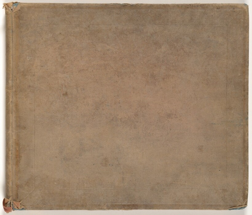 This is a photograph of a closed, aged book with a plain cover. The cover appears worn, with visible marks along the edges and corners, suggesting it has been handled or stored for a long period of time. The color of the cover is light brown. There are subtle lines that could be borders or the edges of a design element. The spine of the book shows folding and fraying at the edges.