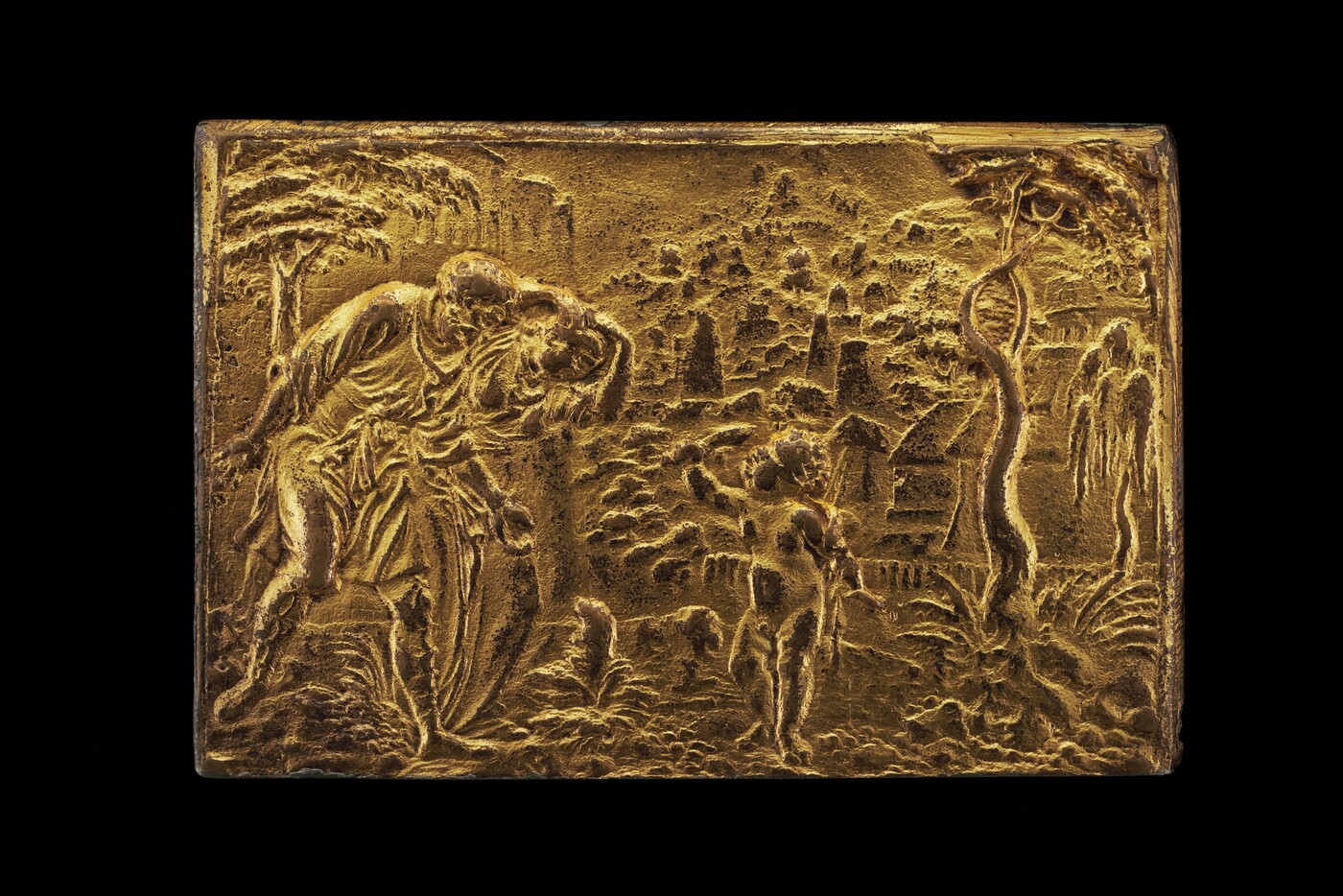 The sculpture portrays a scenic landscape with figures in a narrative setting. The central focus is on two human figures, one of which is an adult guiding a child, as they move through a natural setting. The scene is detailed with surrounding elements such as trees and an architectural structure resembling a small village or castle in the background. The entire sculpture is crafted from gold-colored material, giving it a lustrous and reflective quality. The texture and relief of the sculpture's surface give the figures and landscape depth and dimension, creating a dynamic scene.