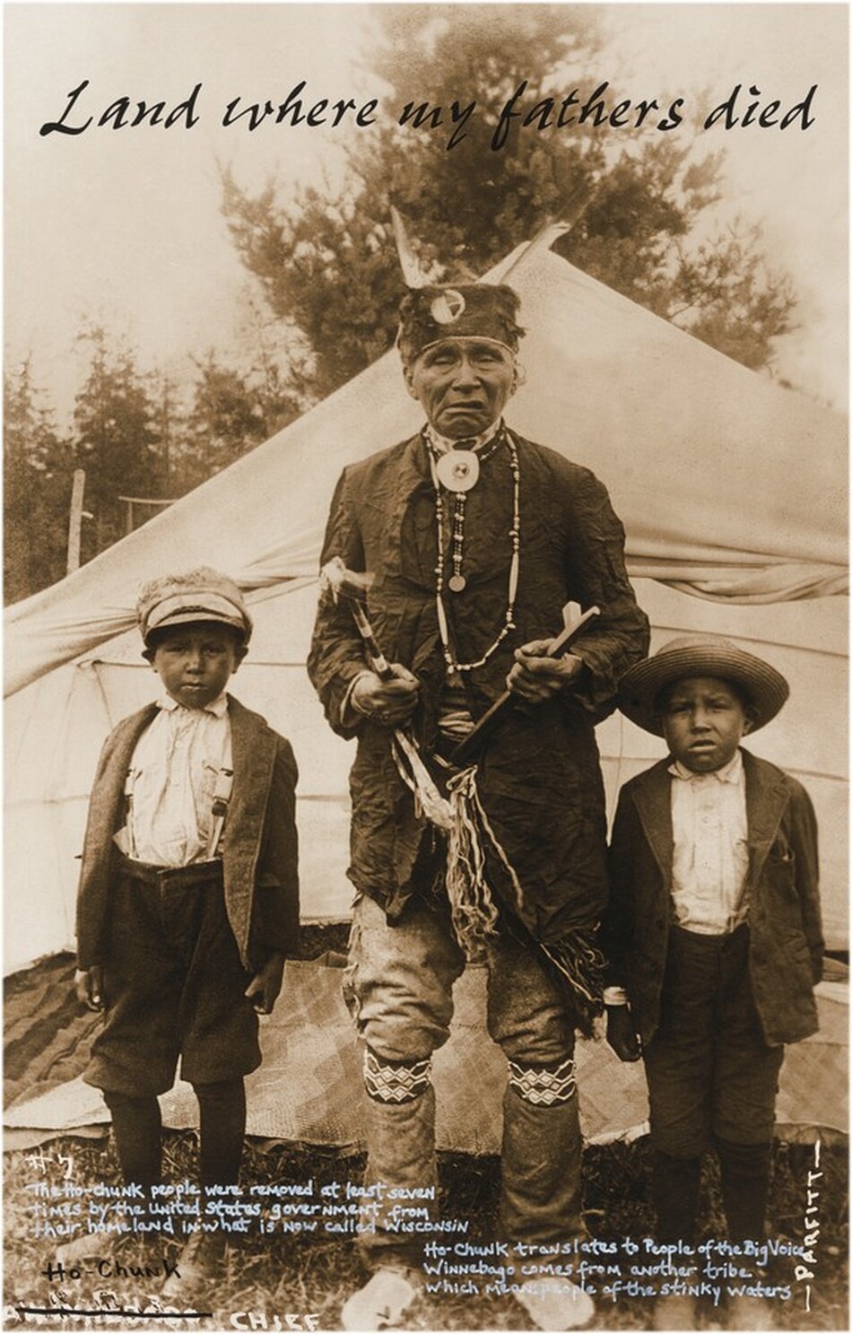 The image shows three people standing upright. The central figure is flanked by two young boys. The central person has distinct facial features, a solemn expression, and is wearing a headband, necklace, dark jacket, patterned leggings, and moccasins. He holds a hatchet in one hand and a staff in the other. The boy to the left wears a cap, light shirt, dark suspenders, and pants. The boy to the right wears a straw hat, light shirt, and dark jacket. The background includes a tent, trees, and textual writing at the top.