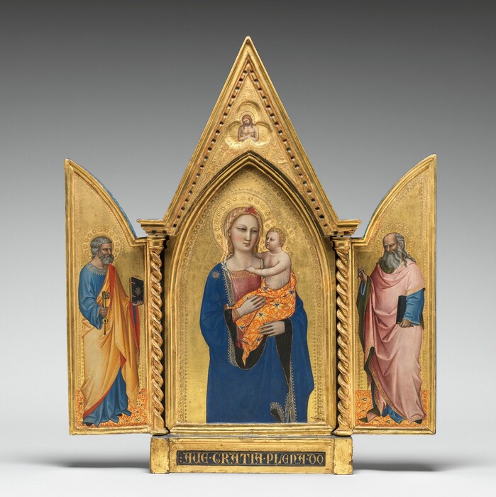 Two panels on a gilded, carved, wooden frame are swung open like shutters to show a bearded, gray-haired man wearing robes standing in each wing, on either side of panel with a pointed, arched top showing a woman holding a baby. In a three-lobed shape in the apex above the woman and child, a nude man crosses his arms over his chest. All the people have pale, ivory-colored skin. Gold halos encircle each person’s head and the background of all three panels is bright gold. The woman in the center panel is shown from the hips up with her body facing us. The deep blue mantle that drapes over her shoulders and her dusty rose-pink dress beneath are trimmed in gold. A sheer veil covers her wavy blond hair and a red, triangular form sits above her forehead like a diadem. She looks to our right with dark, almond-shaped eyes. She has a straight nose, her coral-pink lips are closed, and her smooth cheeks are lightly flushed with pale pink. She holds the child in the crook of her left arm, on our right, and rests her other hand in the baby’s lap. He has short, curly blond hair and looks directly at the woman. He reaches his right arm, farther from us, around his mother’s neck and hooks his other hand in the neckline of her dress. He wears a sheer shirt edged in gold, and the fabric draped around his hips is patterned with tangerine-orange and gold, with lapis-blue clover designs. He has rounded cheeks and a pudgy tummy, but his facial features and arms are scaled more like an adult. Twisted columns separate this central panel from the shutter-like panels to each side. A single person stands in each wing, filling most of the space, and both are angled and look towards the central panel. Both men have darker, olive-toned complexions, wear long robes trimmed in gold, and stand on floors patterned with orange, gold, and sparsely spaced royal blue diamond-shapes. The man to our left has short, steel-gray hair and a trimmed beard. Wrinkles line his forehead, and his brow is furrowed. He wears a topaz-blue, long sleeved garment under a honey-orange robe, the underside of which is ruby-red where it turns back over his wrists and shoulder. He holds a book with a dark cover up in his left hand, farther from us, and a large skeleton key in his other hand. In the right panel, a balding man has a fringe of long, gray hair and a flowing, full beard. His forehead is also creased with wrinkles and his brow is furrowed. The dark, olive-green lining of his rose-pink robe shows where it folds back at his neck, over his wrists, and down the front. His robe covers a topaz-blue garment as well. He holds a book, also with a dark cover, by his side with his left hand, closer to us, and holds up a feather quill with his opposite hand. The inner edges of each of the central panel and both wings are incised with bands of decorative floral and geometric designs punched into the gold backgrounds. In the pointed peak above the central panel, the nude man is shown from the waist up in a three-lobed, clover shape that would be visible even if the wings were closed. The man’s body faces us but his haloed head tips to his right, our left. He has a beard and long brown hair, and a hole dripping blood pierces the back of his left hand, visible on our right. The base of the tryptic is inscribed with gold letters in a dark field: “AVE GRATIA PLENA DO.”