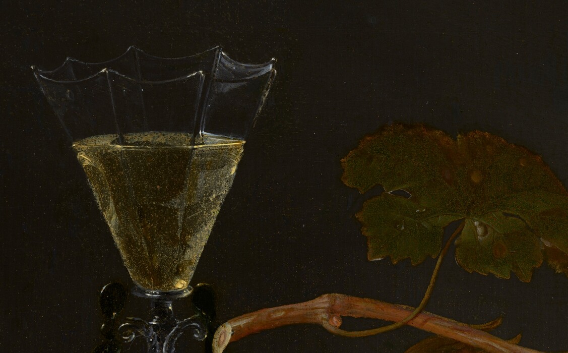 A half-peeled pomegranate, a few nuts, a bunch of purple grapes, and a glass of pale yellow wine sit on the corner of a stone ledge against a dark background in this vertical still life painting. The corner of the chipped gray ledge is close to and lines up with the lower left corner of the painting. Two hazelnuts sit near the front of the ledge, and a twig with three more nuts in papery husks are attached to a twig. Behind that, the flaring cup of the wineglass is made up of flat panels, which are inwardly scalloped along the upper edge, like an upside-down badminton shuttlecock. The stem is made of intertwining ropes of clear and black glass. At the lower center of the composition, the glistening, scarlet-red seeds of the pomegranate contrast with the rust-orange rind. Another twig of hazelnuts is between the pomegranate and the bunch of frosty purple grapes. The vine and a broad, dark green leaf arches over the grapes and pomegranate. The objects are brightly lit from our left against a charcoal-gray background. Molding under the ledge can be made out in the shadows across the bottom edge of the painting. Closer inspection reveals tiny water droplets on the stone ledge and the pomegranate. The artist signed and dated the painting in cursive text on the front face of the ledge, near the lower right corner: “J: Walscappel 1675.”