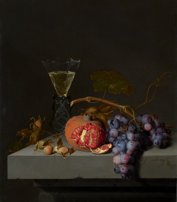 A half-peeled pomegranate, a few nuts, a bunch of purple grapes, and a glass of pale yellow wine sit on the corner of a stone ledge against a dark background in this vertical still life painting. The corner of the chipped gray ledge is close to and lines up with the lower left corner of the painting. Two hazelnuts sit near the front of the ledge, and a twig with three more nuts in papery husks are attached to a twig. Behind that, the flaring cup of the wineglass is made up of flat panels, which are inwardly scalloped along the upper edge, like an upside-down badminton shuttlecock. The stem is made of intertwining ropes of clear and black glass. At the lower center of the composition, the glistening, scarlet-red seeds of the pomegranate contrast with the rust-orange rind. Another twig of hazelnuts is between the pomegranate and the bunch of frosty purple grapes. The vine and a broad, dark green leaf arches over the grapes and pomegranate. The objects are brightly lit from our left against a charcoal-gray background. Molding under the ledge can be made out in the shadows across the bottom edge of the painting. Closer inspection reveals tiny water droplets on the stone ledge and the pomegranate. The artist signed and dated the painting in cursive text on the front face of the ledge, near the lower right corner: “J: Walscappel 1675.”