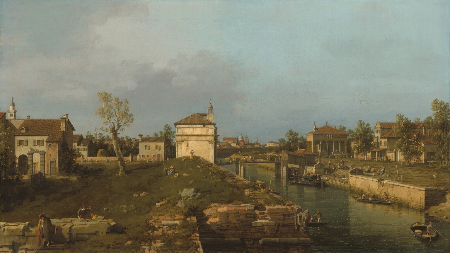 Warm light pours onto white stone and brown brick buildings in a grassy landscape in this horizontal painting. Tiny people walk, stand, sit, and work across the turf, among the buildings, and over a bridge spanning a canal to our right. The people wear long-sleeved shirts, vests, britches, stockings, dresses, hats, and caps in shades of straw yellow, olive green, apple red, muted blue, brown, and bright white. Touches of peach paint suggest they are all pale skinned. The people closest to us are three men working along what might be the remains of a stone foundation in the lower left corner. One raises an instrument while another crouches nearby on the far side of the structure, and the third leans on our side, looking down at the grass. The land rises gently back to the end of a row of structures to our left. A thick-trunked tree with a sparse canopy is halfway between those structures and a building on our side of the bridge, in the center of the composition. That bone-white structure has engaged columns with capitals, a tiled roof, and a round, gazebo-like lantern or bell tower. A brick wall between more buildings line a lane beyond the tree and these structures, and rooflines pile up along the horizon, which comes halfway up the composition. People and children stand and sit on the grassy knoll or walk along the lane. The canal angles from the lower right corner of the canvas to the center of the horizon. The walls of the canal are built with thin layers of peach and tan-colored stone. Close to us, the wall on our side jogs to our left, creating an inlet or bay. A staircase cuts into the far wall to allow access to the water. Boats steered by men using long sticks carry people or supplies. A more elaborate covered boat, likely a ferry, pulls up to the base of the stairs. The stairs lead up to a plaza, which is lined with peanut-brown buildings with terracotta-brown roofs. People and dogs mill about the square and cross the bridge beyond the ferry. Some smoky-purple clouds drift into the scene from the left against an otherwise clear blue sky.