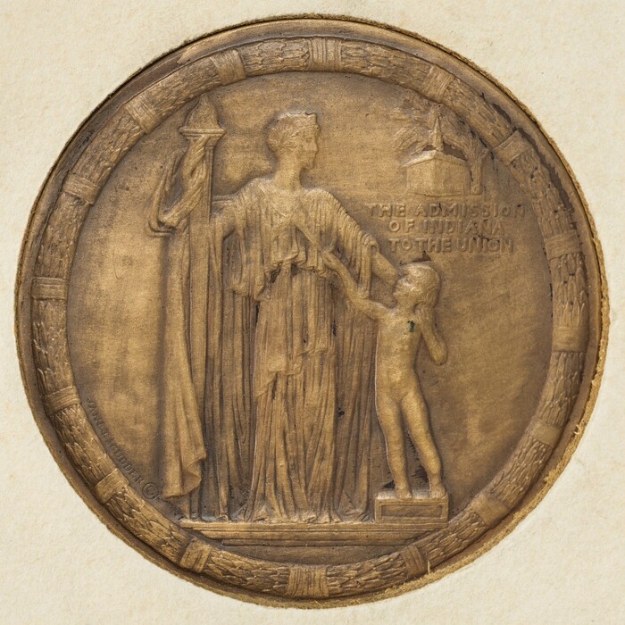 The sculpture is a circular relief medallion featuring two figures. The central subject is a robed figure holding a torch in her right hand. Beside her is a smaller figure standing on a pedestal reaching towards the torch. The figures are depicted in a classical style, with the larger figure dressed in a draped garment. The medallion is bronze in color, suggesting it is made from a metal like bronze. The border of the medallion has an intricate, woven pattern. Inscribed to the right of the figures are the words "THE ADMISSION OF INDIANA TO THE UNION." The sculpture is detailed and skillfully rendered.