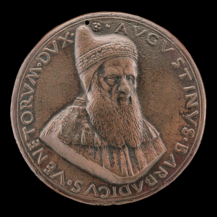 The image depicts a round sculptural medallion with a relief portrait of a man with a long beard and a headpiece resembling a beret or turban. The material appears to be bronze with a brownish patina. The portrait is in a three-quarter view, facing towards the viewer, showing facial features and textured clothing details. Surrounding the portrait is text inscribed in a circular format on the medallion's rim.