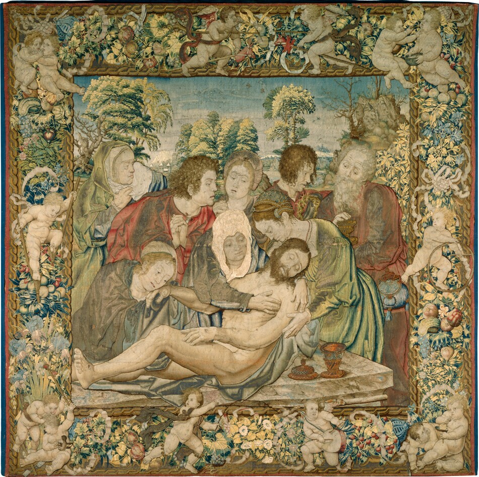 Five women and three men gather around the limp, nude body of a man being laid on a stone slab in this square tapestry. The people’s skin is pale, nearly ivory white. The torso of the dead man, Jesus, is being supported by two women, one of whom wraps her arms around his shoulders. The man has a brown beard and hair, and his eyes are slightly open. He has holes in the hand and foot we can see and a gash over his right ribs. A silvery blue cloth is between Jesus and the stone surface, where a copper-colored ointment jar sits with the lid off near the front right corner. The woman embracing him has a white head covering and lapis-blue and white dress. The other woman supporting his torso, to our right, wears a dress that shimmers between frosty lemon-lime green and cobalt blue. Her strawberry blond hair is braided, wrapped around her head, and ornamented with pearls. A third woman to our left bends over and touches Jesus’s far hand to her cheek. She and the others standing in a row behind this group wear robes in tones of slate blue, pale green, blue, and rose red, though some areas appear gray with damage or wear. Behind Jesus and these three women are two more women and three men. They all look on except one woman and man, who look at a chalice a man standing to the right holds. That man has a long gray beard and hair, and a pouch hangs at his waist. The man next to him holds a ring of thorns. The landscape beyond the group has trees with yellow-highlighted and blue-shaded trees and distant buildings and mountains under a blue sky. The scene is framed by an ornamental design of chubby, pale-skinned baby boys playing games amid fruit, flowers, and ribbons. Two boys at the top play with hobby horses. To the right, one child feeds another as a third plays with a stick and chest-high hoop. A boy blows bubbles in the lower right corner, and another plays a drum nearby. A boy with rings of bells wrapped under his knees runs toward the drummer. Two in the lower left corner have captured a bird, and another above them walks on stilts.