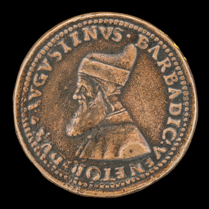 The image shows a sculpted coin featuring the profile of a man in relief, facing to the left. The subject wears a tall hat and has a pointed beard. The coin has a round shape and a rich brown color. Surrounding the central figure is an inscription which reads "AVGUSTINVS BARBADICO VENETOR. DVX." The details on the coin, such as the facial features and the texture of the beard, are sharply defined against the flat background. The coin's edge is bordered with a series of small, evenly-spaced raised dots.