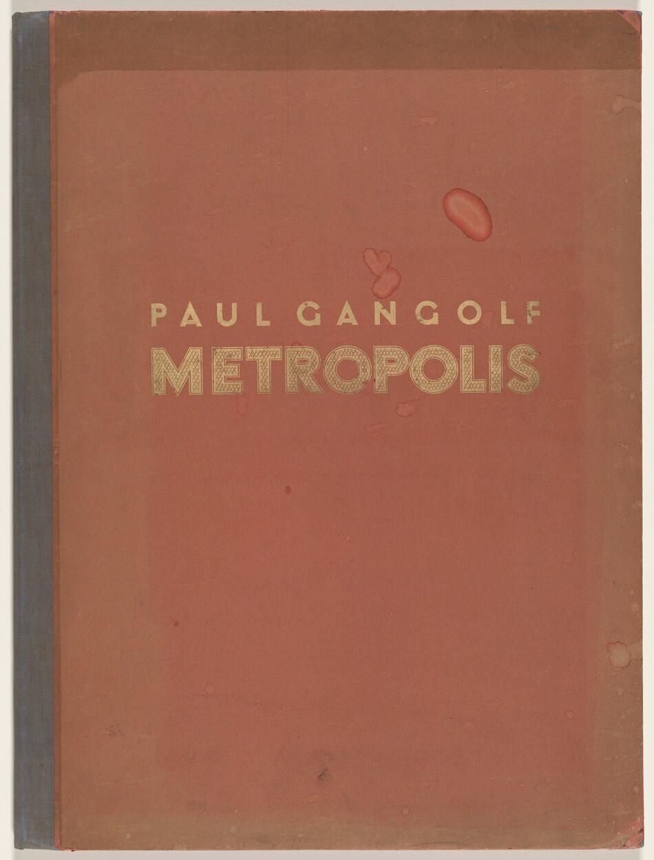 This is a photograph of a book cover. The cover is primarily a reddish-brown color with a subtle gradient, textured with various stains and smudges. The spine of the book is a darker shade. Centered on the cover are the words "PAUL GANGOLF" and below it, in larger font, "METROPOLIS," both in a gold-colored, bold typeface.