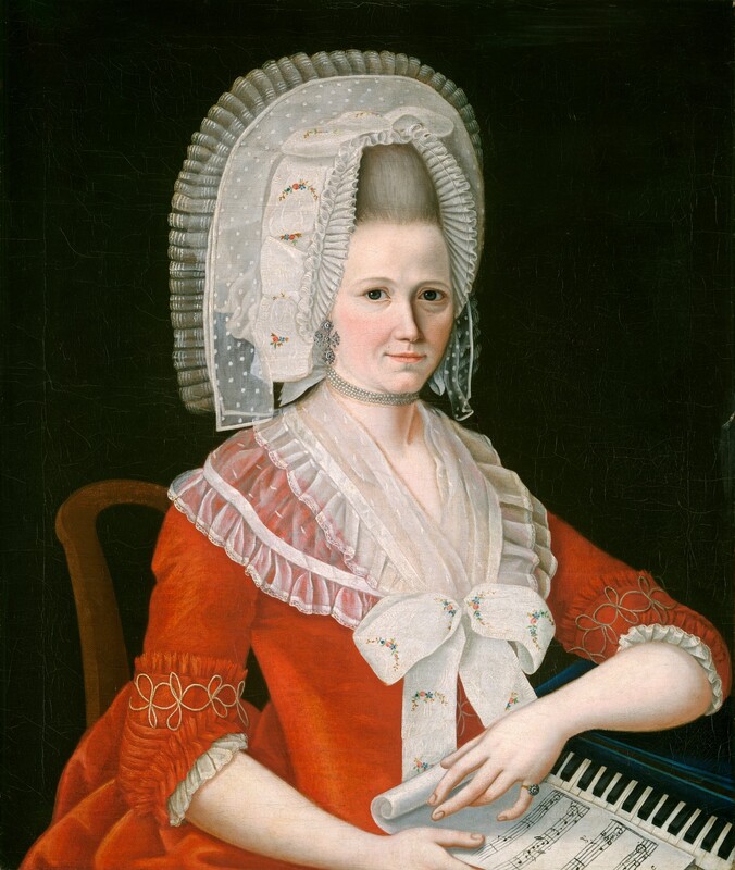 Shown from the waist up, a pale-skinned woman wearing a ruby-red dress and voluminous, pleated white headdress sits against a dark background in this vertical portrait painting. The woman’s body is angled to our right, but she looks at us from the corners of her dark gray eyes. She has thin eyebrows, lightly flushed cheeks, faintly smiling lips, and a wide, cleft chin over a slight double chin. A flesh-colored mole is just above the left corner of her mouth. Gray hair is swept up under the upside-down U-shaped headdress, which is pleated with translucent white fabric along the front and up and over the back. Another ribbon is solid white with a blue, red, and yellow floral pattern, and another is dotted with solid white against transparent fabric. The earring we see is a silver, ornate cross shape, and four strands of tiny pearls are tight to her neck like a choker. More translucent white cloth, now edged in ruffles, wraps around her neck and shoulders and is gathered under a bow tied with more of the floral-patterned ribbon. The vivid red dress has elbow-length sleeves with a looping gold design near the cuffs. White ruffles peek beyond the edges of the cuffs, and she wears a ring on the pinky finger of her left hand. The bodice is tightly fitting, and the skirt bunches up behind the woman in the wood chair, the back of which curves just beyond her right shoulder, to our left. She unfurls a scroll of music with one hand and holds the sheet with the other. Her left elbow, to our right, rests on the top of a narrow, black keyboard. The background is nearly black.