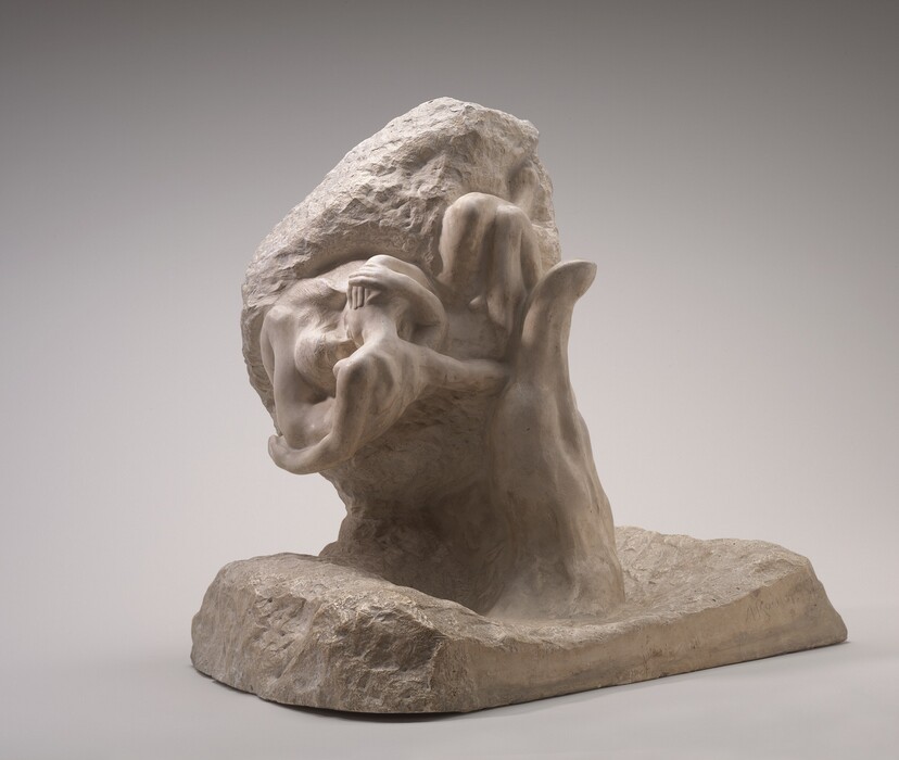 A hand cupping two nude people, which are significantly smaller in scale than the hand, rises from a rectangular base in this oatmeal-colored, free-standing plaster sculpture. The roughly textured base is angled away from us to our right, so we look into the hand holding the intertwined people with the well-defined thumb to our right. The woman’s body is curled in a U shape, with the back of her shoulders facing us. The man rests his head against her breast as they kiss, and he wraps both arms up around her head. His legs extend to our right, his knees bent and pressed together. His right hip nestles in the curve of the thumb. The area around the people is roughly textured while the hand and most of their bodies are polished smooth. The artist inscribed his name in the lower right corner of the base, “A Rodin.”