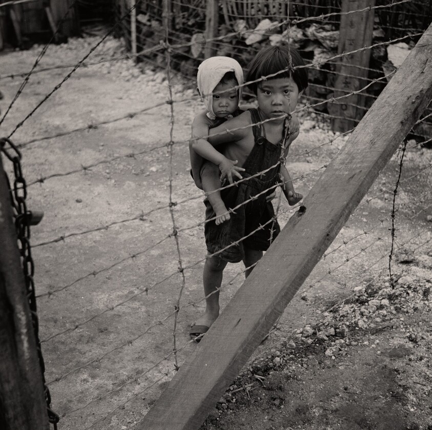 Child with Infant on His Back behind Barbed Wire. Prison for Suspected Collaborators, Guam