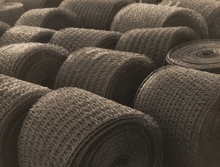 The image shows multiple large rolls of wire mesh in a uniform pattern. The color palette is sepia tones, giving it a vintage appearance. The rolls are arranged in rows, extending from the bottom left to the top right of the image, with each subsequent row slightly elevating in the background.