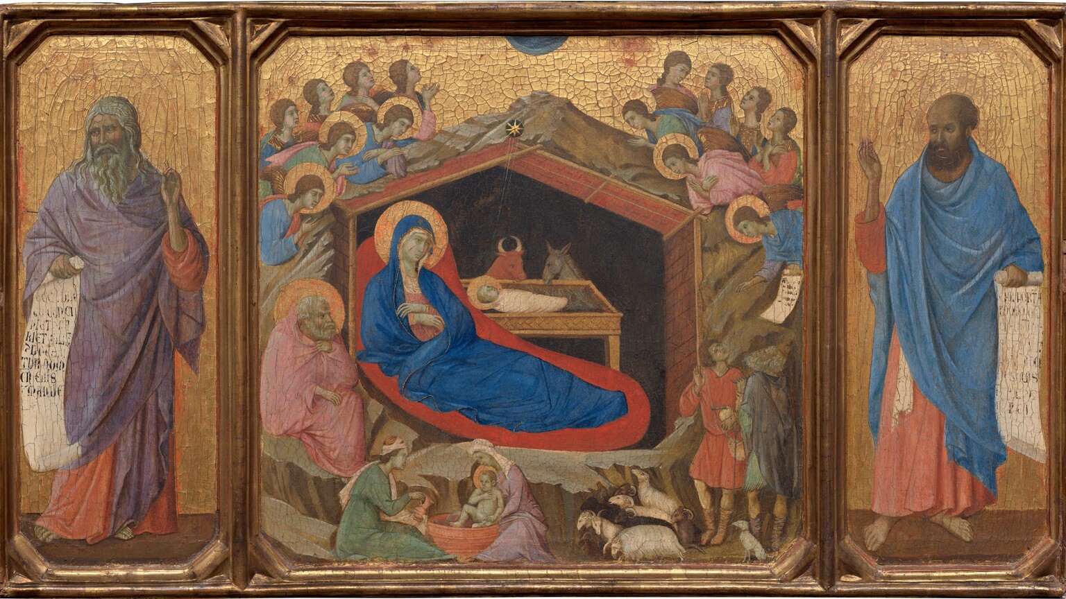 This horizontal painting is made up of three parts: in the center square panel, a woman reclines under a wooden shelter set into a rocky cave, which is surrounded by angels, and narrower wings to either side are each occupied by a standing man. All the people have pale skin, which is tinged with faint green. The three panels are joined with a gold frame, and the gold background behind the central scene and the men in the side panels are covered with a noticeable network of cracks. In the central panel, a cobalt-blue robe nearly envelopes the reclining woman’s body; this is Mary. It covers her head and falls open where she crosses her wrists over her chest to show a pink garment underneath. A flat gold halo encircles her head ,and her body is surrounded by a field of crimson red, almost like an aura. She rests under a wooden structure with a pitched roof, which is surrounded by craggy, barren rock. A swaddled infant lies in a rectangular, tray-like manger. The infant’s head is also surrounded by a gold halo. Fine gold rays emanate down into the structure from a star just above the peak of the roof. A bull and a donkey look down at the baby from the far side of the manger. The interior of the structure behind them is black. In a smaller scale, two women wash a haloed infant in a tub in front of the rocky cave near the lower left corner of this panel. A man with a white beard and hair sits to our left of Mary, holding a pink cloak at his throat and looking toward the infant. Above and around the rocks, seven winged and haloed angels cluster on each side. One angel to the right presents a scroll with black writing to two men accompanied by a dog and several sheep in the lower right. The man in the panel to the left, Isaiah, has a gray beard and long, wavy hair, and he wears a lilac-purple cloak draped over a coral-orange robe. In his right hand, on our left, he holds an unfurled scroll with large black lettering. His other hand is raised with one finger pointing upward. He looks to our left, away from the central scene. On the right, Ezekiel, echoes Isaiah's pose. Ezekiel holds an open scroll with his left hand, on our right, and his other hand is raised. He also wears a coral-colored robe, but his is overlaid with a blue cloak. His receding hair is short and brown, as is his beard. Like Isaiah, he takes up most of the height of the panel and gazes to our left, toward the central panel.