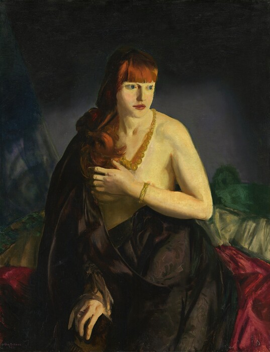 Shown from the knees up, a woman sits partially covered by a black cloth as she holds one forearm across her bare breasts in this vertical painting. The woman has pale, yellow-tinged skin and long, copper-red hair and bangs. Her body faces us, but she turns her head to look off to our right with large blue, wide-set eyes. Her cheeks are flushed, and her full, dark pink lips are closed. A strand of gradually larger amber-yellow beads hangs around her neck, and she wears a gold-colored bracelet on the arm braced across her chest, her left arm, to our right. Glimpses of pale pink nipples are visible. The voluminous black cloth drapes down over one shoulder and across her hips. She wears a ring on the other hand, which emerges from the cloth to rest on that knee. Piles of garnet red, peridot green, and forest green are piled up to chest height behind her, and the background is nickel gray around her body and darkens to black around the top and side edges. The scene is loosely painted, especially in the fabric and background. The artist signed the canvas in the lower left corner, “Geo. Bellows E.S.B.”