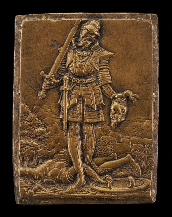 The sculpture shows a warrior standing over a fallen opponent. The warrior wears detailed armor, holds a sword in his right hand, and the opponent's severed head in his left hand. The scene is on a bronze plaque. The warrior looks strong and dominant, with intricate armor and facial features. The fallen opponent lies below the warrior, partially covered by the warrior's cape. In the background, there are trees and rolling hills.