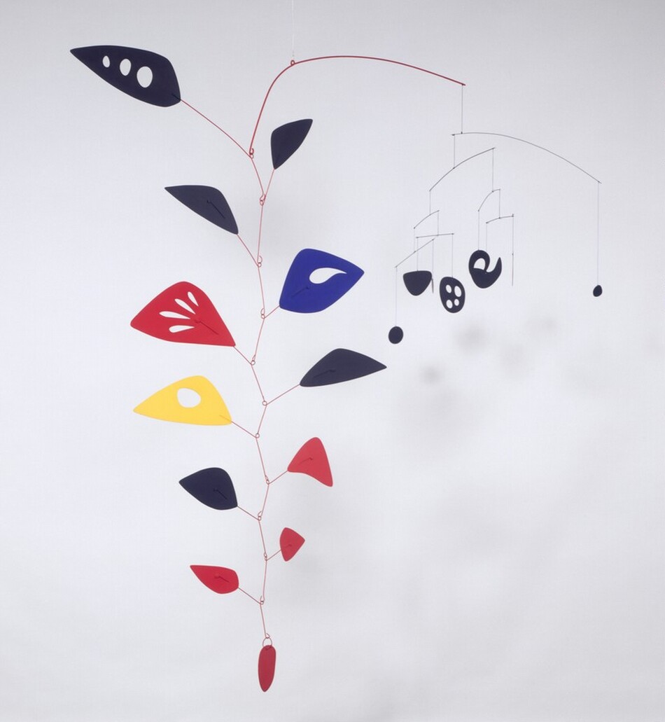 This free-floating sculpture, called a mobile, hangs from the ceiling and branches into two separate, vertical sections that hang from a shared wire. To our left, the larger part of the mobile is made of twelve flat, uniquely shaped paddles suspended on curving, painted wires in bowing, branch-like forms. Three black, leaf-like shapes are clustered at the top over a royal-blue form, a lemon-yellow form, two more black shapes, and five crimson-red shapes that get smaller as they get closer to the bottom. They are loosely spaced but hung to taper like a bunch of grapes. To our right, a second smaller set of branches and shapes, like a mini mobile, is made of seven branches. In this photograph, five of the rounded, black shapes hanging from the dangling wires face us and the others are seen from their edge, so appear as vertical lines.