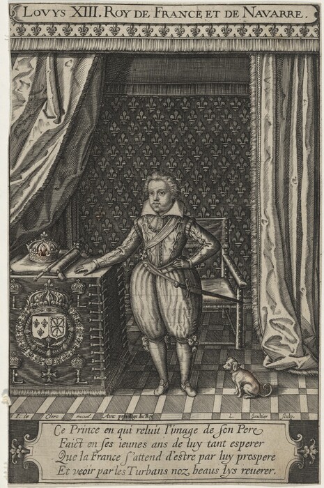 The image shows a young royal figure standing. The person has one hand on a cushioned table and the other hand on their hip. The individual has a neutral expression and styled, wavy hair. They are wearing royal attire including a doublet, puffed breeches, knee-high boots, a sash, and a belt. Beside them on the table is a crown, a rolled document, and regal emblems. In the room, there is a high-backed chair and a small dog near the person. The background features an ornate tapestry with fleur-de-lis motifs and richly decorated drapery.