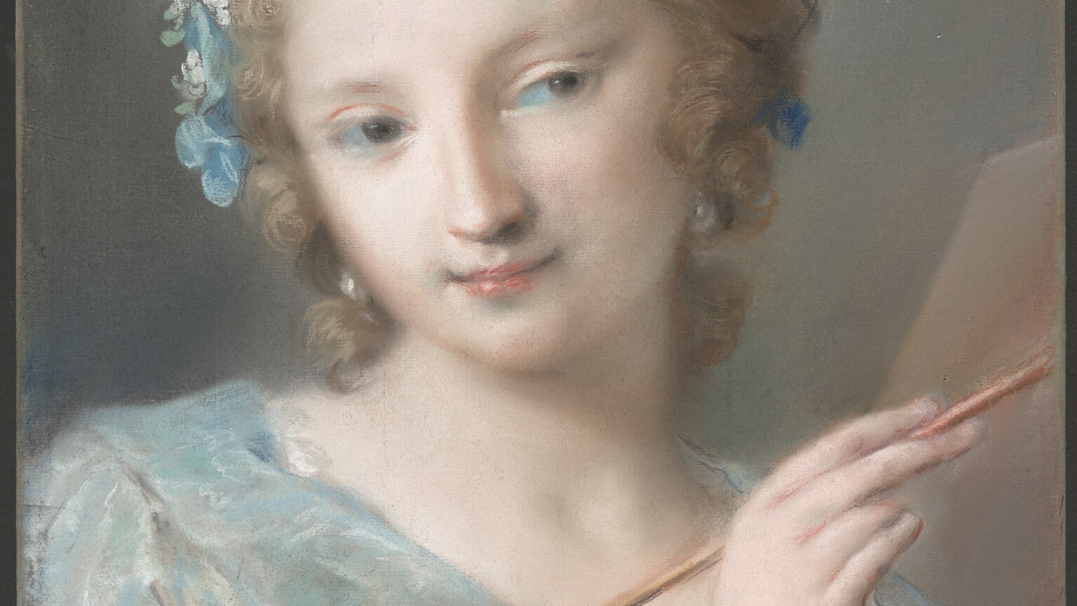 Shown from the chest up, a young woman with pale, smooth skin and dressed in a light blue gown holds a paint brush and palette in this vertical pastel drawing. The woman’s body is angled to our right. She turns her head back to our left but then looks back off to our right from the corners of her eyes under faint brows. Her wide-set eyes are gray, her nose long and straight, and her delicate pink lips are closed in a slight smile. Her curly, ash-blond hair sweeps back from her forehead to gather in a braid across the crown of her head. Soft, loose tendrils frame her round face, which has touches of ice-blue shadows at the corners of her mouth and eyes. Sky-blue and white flowers with mint-green leaves adorn her hair to our left, and two touches of royal blue near her ear on our right suggests a ribbon. Gleaming white pearl earrings hang from her ears. Her dress is created with filmy layers of arctic blue, taupe, white, and pale pink. The gown has a deep, V-shaped neckline, and a long sleeve is turned back from the wrist we can see. In that hand, she holds the wooden paintbrush at about chest height, and it extends off the right edge of the sheet. In the lower right corner of the composition, the thumb of her other hand hooks through a hole in the palette, which has daubs of pink and white. The corner of a blank easel is visible over her shoulder to our right. The background is mouse gray tinged with the blue of the paper on which it is drawn.