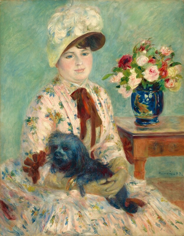 Shown from the lap up, a pale-skinned woman wearing a floral-print dress holds a black lap dog in this vertical portrait painting. The woman’s body is angled to our right, and she gently smiles as she looks slightly down in that direction with blue eyes. She has a round face, rosy, smooth cheeks, pale pink lips, and a double chin. Her brown hair is mostly covered by a hat with a brown brim and pale yellow crown. A bloom of white feathers nestles at the top front of the hat. Her dress is pale pink with a floral pattern painted with dabs of yellow, red, blue, and green. A burgundy-red bow is tied around her neck and lies limply down her chest. The woman wears gold bracelets over pale olive-green gloves that stretch almost to her elbows. Her fingers are interlaced as she holds the shaggy black dog in her lap. The dog’s front paws rest over the woman’s right forearm, to our left. A table in the background to the right holds a wide-mouthed, lapis-blue vase painted with a yellow and orange bird and white flowers. The vase holds at least a dozen pink, red, and white flowers and greenery. The background is painted with strokes of turquoise and mint green. Some brushstrokes are visible, as in the flowers and the woman’s dress, and some brushstrokes are blended, as in the woman’s face. The artist signed the painting near the bottom right corner, “Renoir 83.”