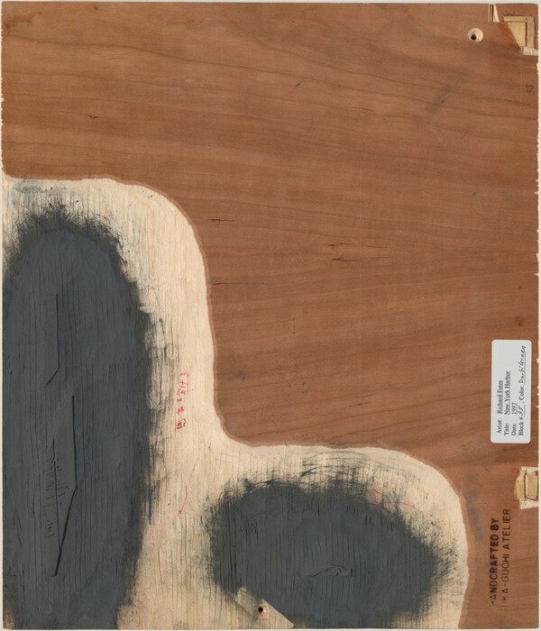 The image shows bold and irregular shapes on a wooden surface. Two abstract dark forms contrast with the textured wood grain, which is smooth and honey-brown. The shapes might evoke natural elements or islands from above, with muted tones resembling water. A label and printed text are visible in one corner.