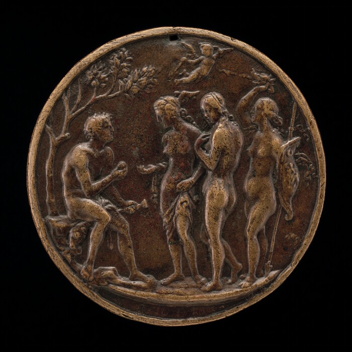The sculpture is a circular bronze medallion depicting a scene with four figures in a relief. On the left, a seated man looks up at three standing women to his right. The women appear to be engaged in conversation or a presentation, with one of them holding a staff and shield. Above the group, there is a small winged child flying over the scene. In the background are the leaves of a tall tree. The sculpture appears bronze with areas of darker patination.