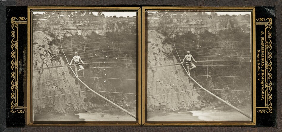 This is a stereoscopic image showing a person walking on a tightrope over a gorge. The scene features a tightrope extended over a natural gorge with rocky cliffs and a river below. Safety lines are visible above and around the tightrope. The background shows a natural landscape with trees and rocky formations. The image is presented in an ornate frame and the person appears to be wearing traditional attire.