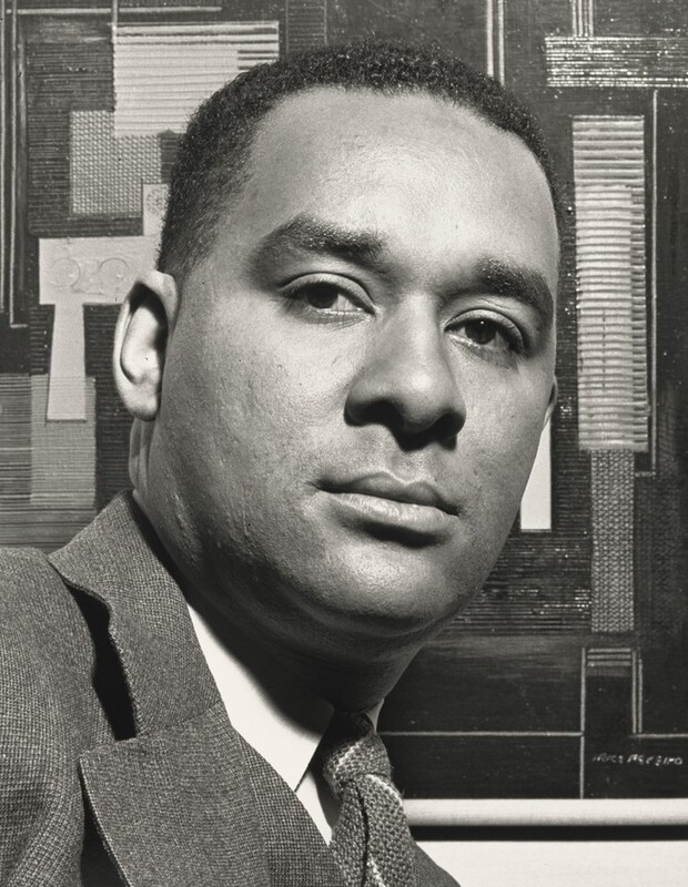 The face and top part the shoulders of a Black man take up most of this vertical black and white photograph. The man’s chest faces our right, but he turns to look at or just past us with dark eyes. His chin tips slightly up so his eyelashes cast shadows onto his lower lids. He is cleanshaven with wide eyebrows, a square-shaped face, and a slight double chin. His hair is cut short, and he wears a suit jacket over a white collared shirt and tie. The background is filled with an abstract composition of overlapping geometric, mostly rectangular shapes and lines. The work of art is signed in the lower right corner but is illegible in this photograph.