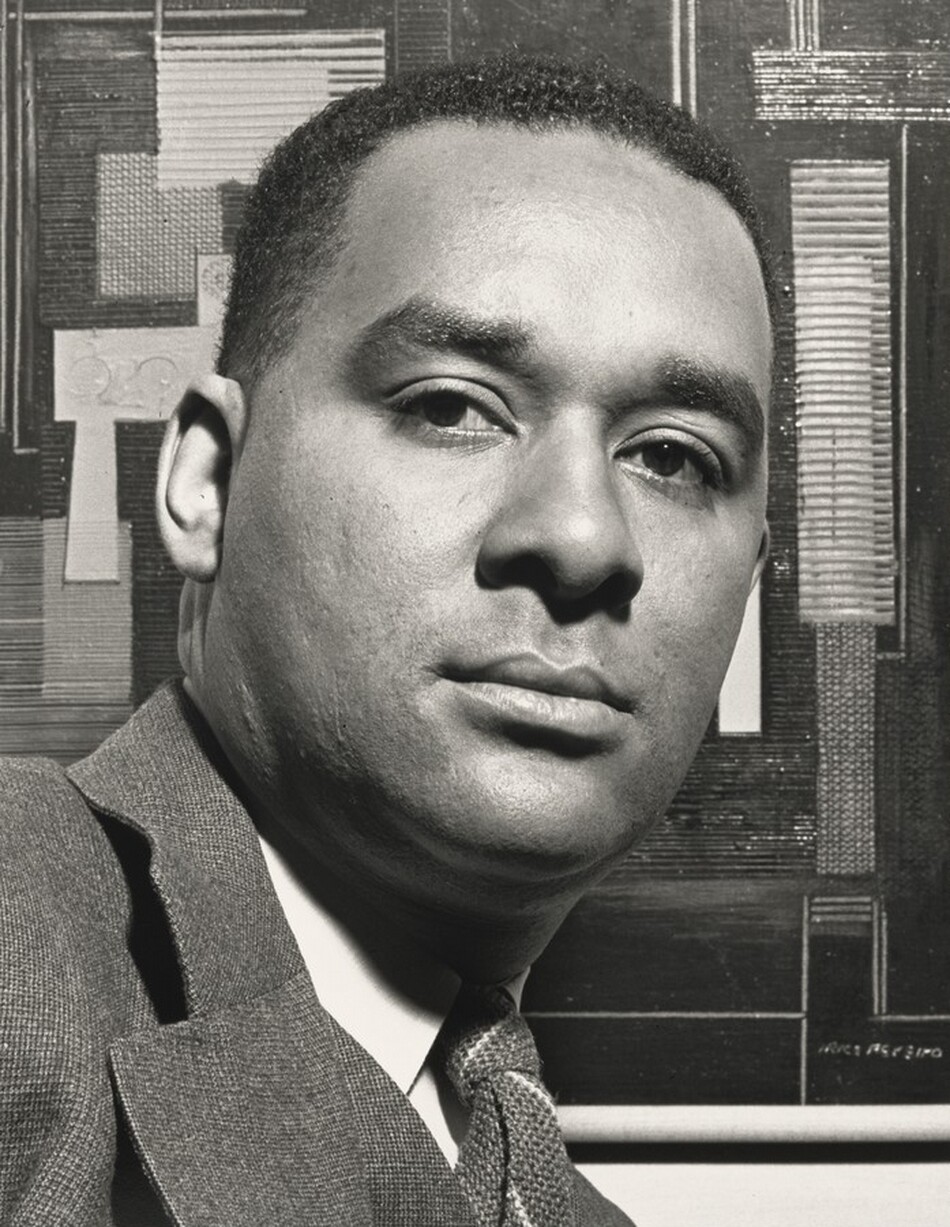 The face and top part the shoulders of a Black man take up most of this vertical black and white photograph. The man’s chest faces our right, but he turns to look at or just past us with dark eyes. His chin tips slightly up so his eyelashes cast shadows onto his lower lids. He is cleanshaven with wide eyebrows, a square-shaped face, and a slight double chin. His hair is cut short, and he wears a suit jacket over a white collared shirt and tie. The background is filled with an abstract composition of overlapping geometric, mostly rectangular shapes and lines. The work of art is signed in the lower right corner but is illegible in this photograph.
