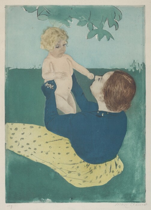 The image shows an adult and a child in an outdoor setting. The adult is seated, while the child is held upright on their lap. They are surrounded by grass and there are leafy branches above them, suggesting they may be under a tree. The adult has long brown hair and is wearing a blue top and a yellow skirt. The child has short, curly, blonde hair and appears nude.