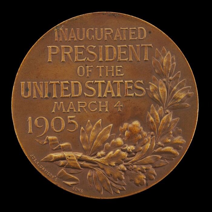 The sculpture is a circular commemorative medal marking the inauguration of the President of the United States. The surface is inscribed with the words "INAUGURATED PRESIDENT OF THE UNITED STATES MARCH 4 1905," along with decorative elements like olive branches and possibly laurel leaves. The color of the sculpture is a rich brown, suggesting a bronze material. It presents a flat, round form with text and decorative elements in relief, highlighting its purpose as a commemorative or historical artifact.